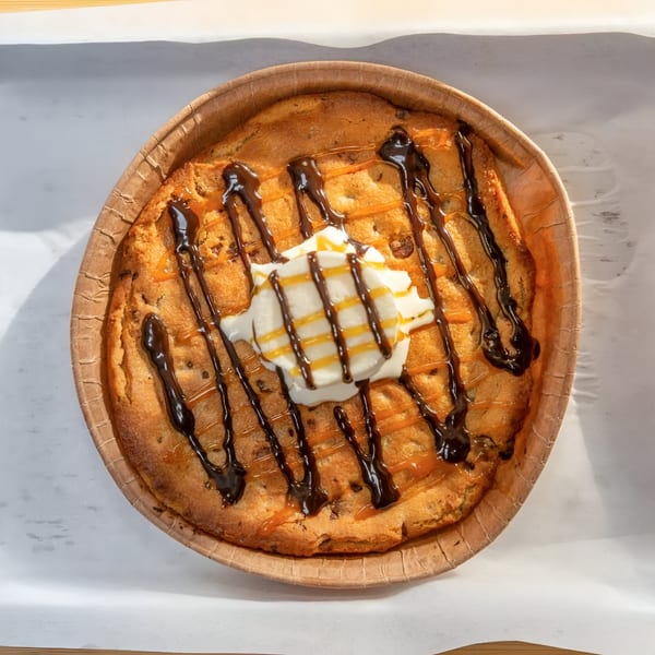 A dessert pizza with chocolate and caramel drizzle, topped with a dollop of whipped cream.