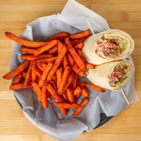 A chicken bacon ranch wrap, cut in half, served with a side of sweet potato fries.