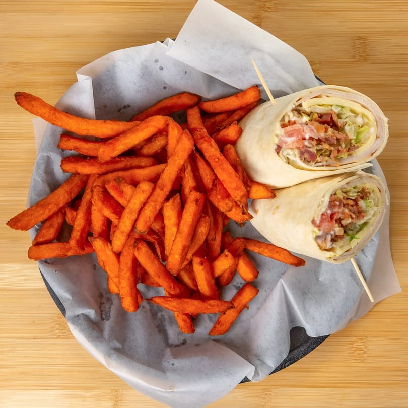 A chicken bacon ranch wrap, cut in half, served with a side of sweet potato fries.
